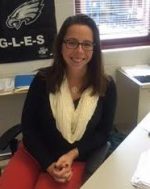 AP economics teacher Kieran Sweeny sits at her desk welcoming students into her classroom.