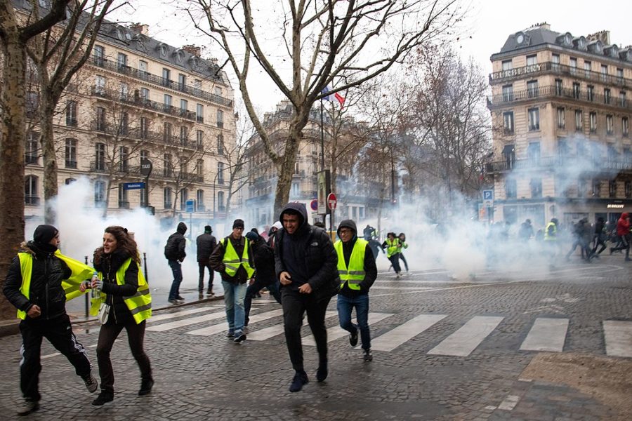 The gilet jaunes (Yellow Vests) run the streets of France in the midst of the fire smoke. The yellow vest is a symbol of civilian resistance to the raise of fuel taxes and other issues deemed problematic. (Photo obtained via Wikipedia.com under a Creative Commons license)