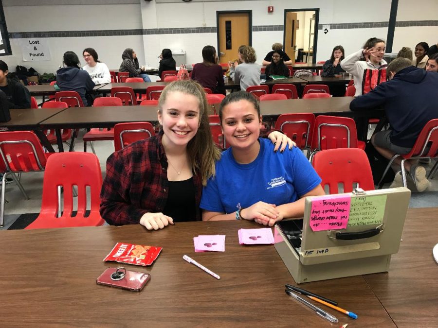 Armonia Choir member, sophomore Francesca Bellora (left), and Armonia and Madrigals Choir member, sophomore Elizabeth Hughes (right), sit in the cafeteria as they manage the Singing Valentines sales. Singing Valentines are for sale for $5 a song. (Photo by Zach Anderson)