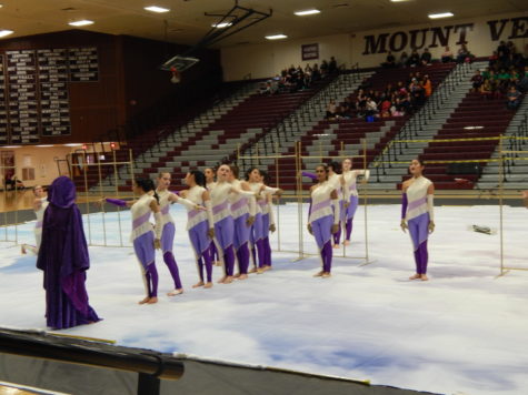 The Red Winter Guard team lines up behind the Gatekeeper. The Gatekeeper is clothed in purple robes and represents the key to eternity. 