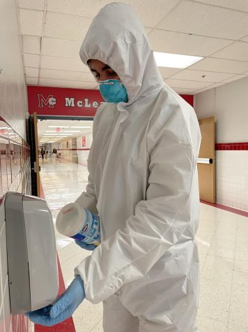 Senior Arman Nikmorad cleans a hand sanitizer dispenser in the hallway. Upon returning to school, some students wore hazmat suits to protest against in-person learning.