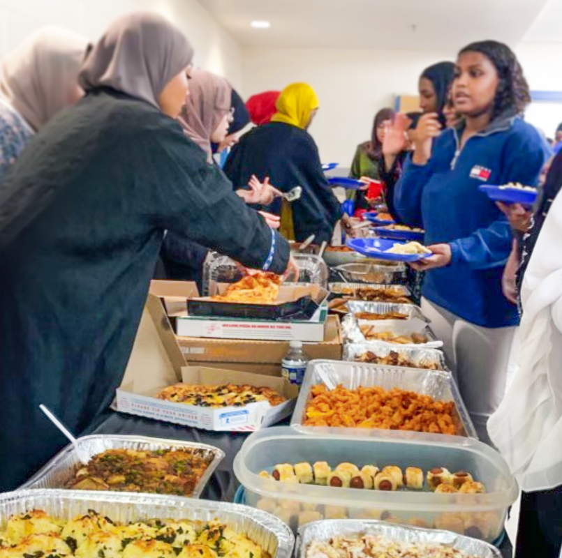 Attendees+of+the+2023+annual+MSA+iftar+event+grab+food+for+their+plates+to+end+their+fast+for+the+day.+Students+brought+a+variety+of+food%2C+some+representing+their+cultural+cuisines.+