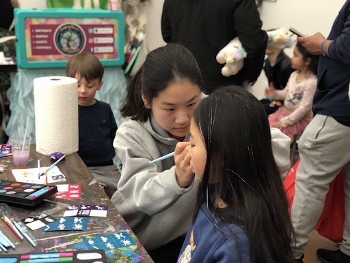 Rotary Club president Chloe Jeong helps face-paint a child attending the festival. Volunteers from the McLean Interact Club had the opportunity to communicate with children from the community.