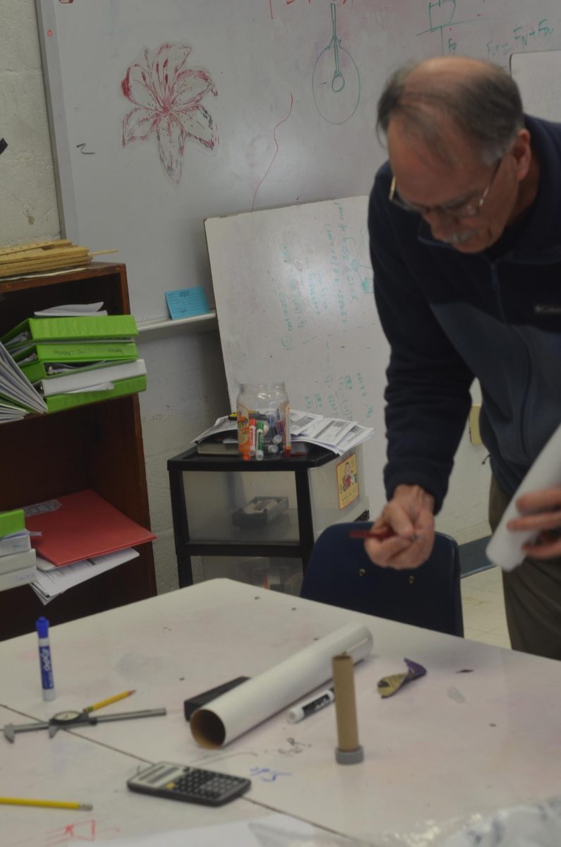 National Rocketry Association mentor Steve Morris precisely measures and cuts a tube of cardboard for the fuselage of the rocket. The diameter of the body is exactly 2.2 inches for aerodynamics.