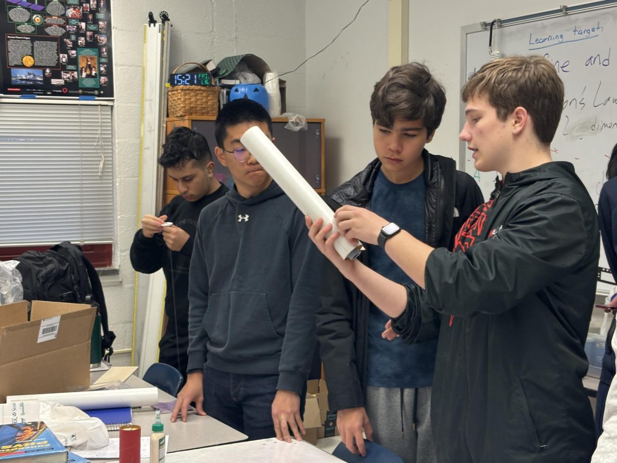 Sophomore Everett Munson holds up the fuselage of the rocket and explains the construction of the body.