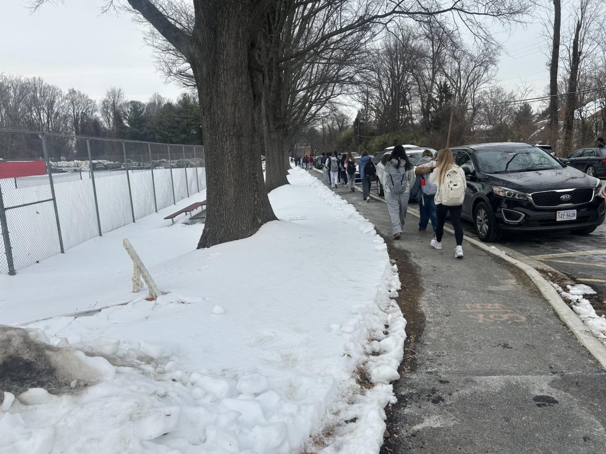 Students cautiously leave school after their first day back from the winter storm, careful of the icy sidewalks. Snow is piled up around the fields, parking lots, and walkways.