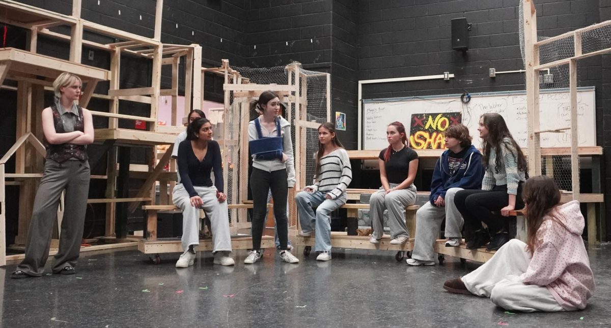 The cast of TheatreMcLean's Men On Boats scatter across the set, practicing their lines. Men On Boats features many "rapids" scenes, which involve periods of short, intense dialogue scenes while the crew attempts to keep their boats under control in the water. These scenes take extra review due to the rapid fire nature of the line delivery.